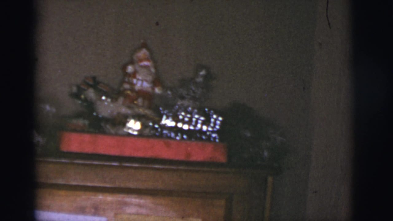 1966 Tucson home-movie frame showing a wooden mantel or cabinet topped with shiny holiday decorations and a Santa figure.