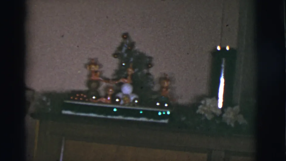 1966 Tucson home-movie frame showing a small Christmas tree, figurines, garland, and a candle holder on a mantel.