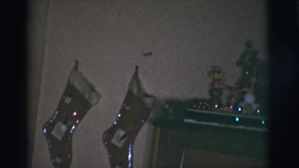 1966 Tucson home-movie frame with two hanging Christmas stockings beside mantel decorations and a small tree.