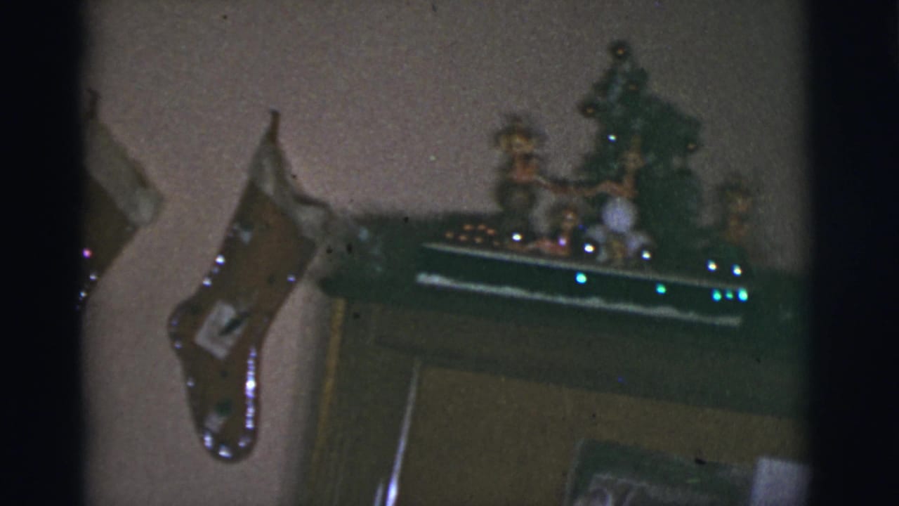 1966 8mm home-movie frame from Tucson, Arizona, showing handmade Christmas stockings near a mantel display in a private home.