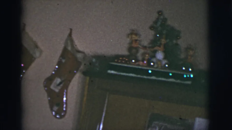 1966 8mm home-movie frame from Tucson, Arizona, showing handmade Christmas stockings near a mantel display in a private home.