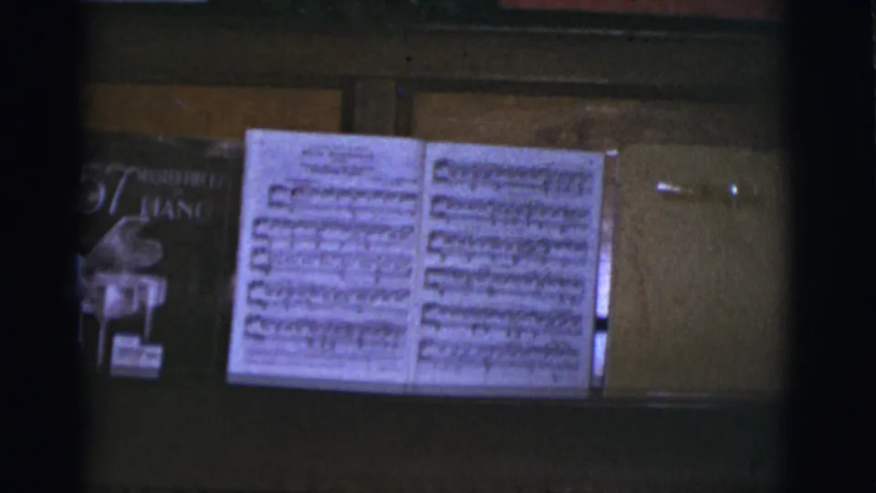 Tucson, Arizona 1966 home-movie frame with open sheet music and a visible piano anthology on an upright piano in a private Christmas setting.