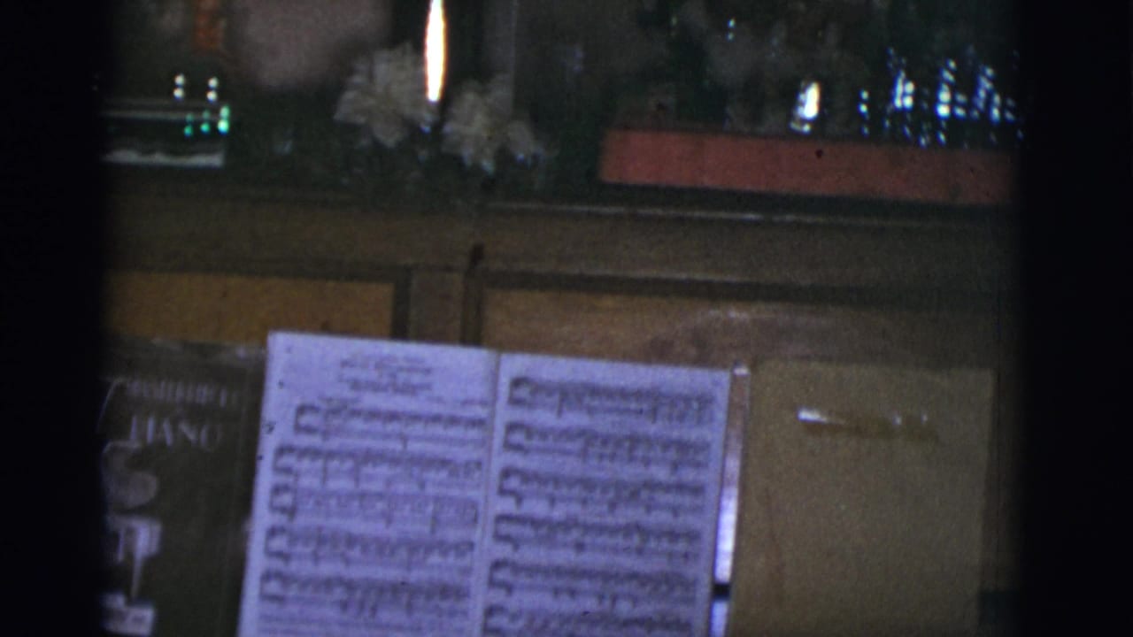 Open sheet music on a piano with holiday decorations in dim interior light.