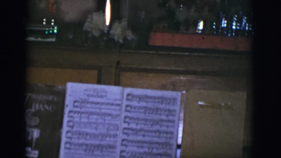 1966 Arizona home-movie frame showing open sheet music on a piano beside small Christmas decorations in a private interior.