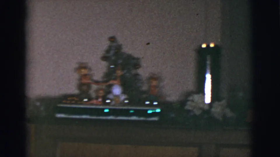 1966 Arizona home-movie frame of a decorated piano top with figurines, a tall candle, flowers, and a compact Christmas display.