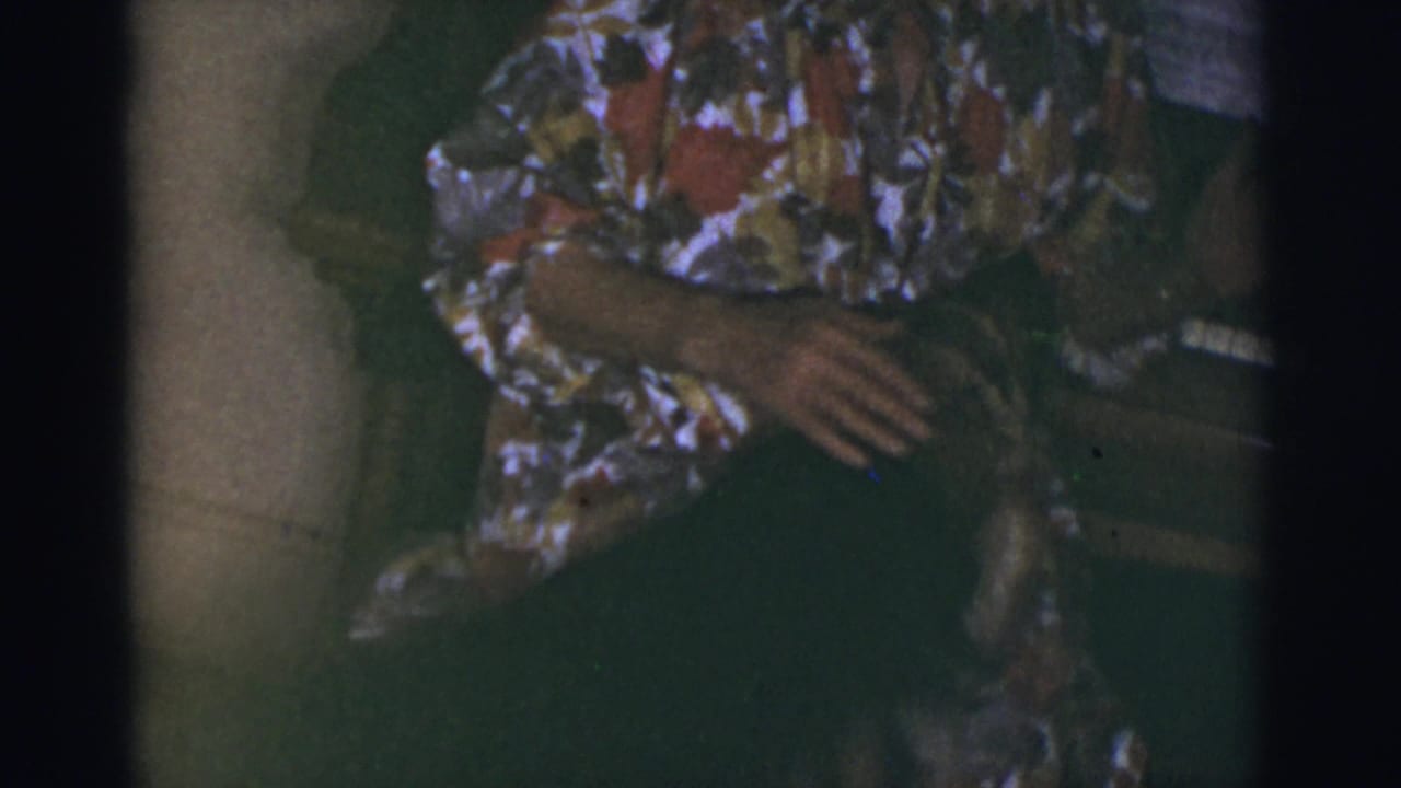 Seated woman rests one hand near a dark shape in the foreground beside the piano.