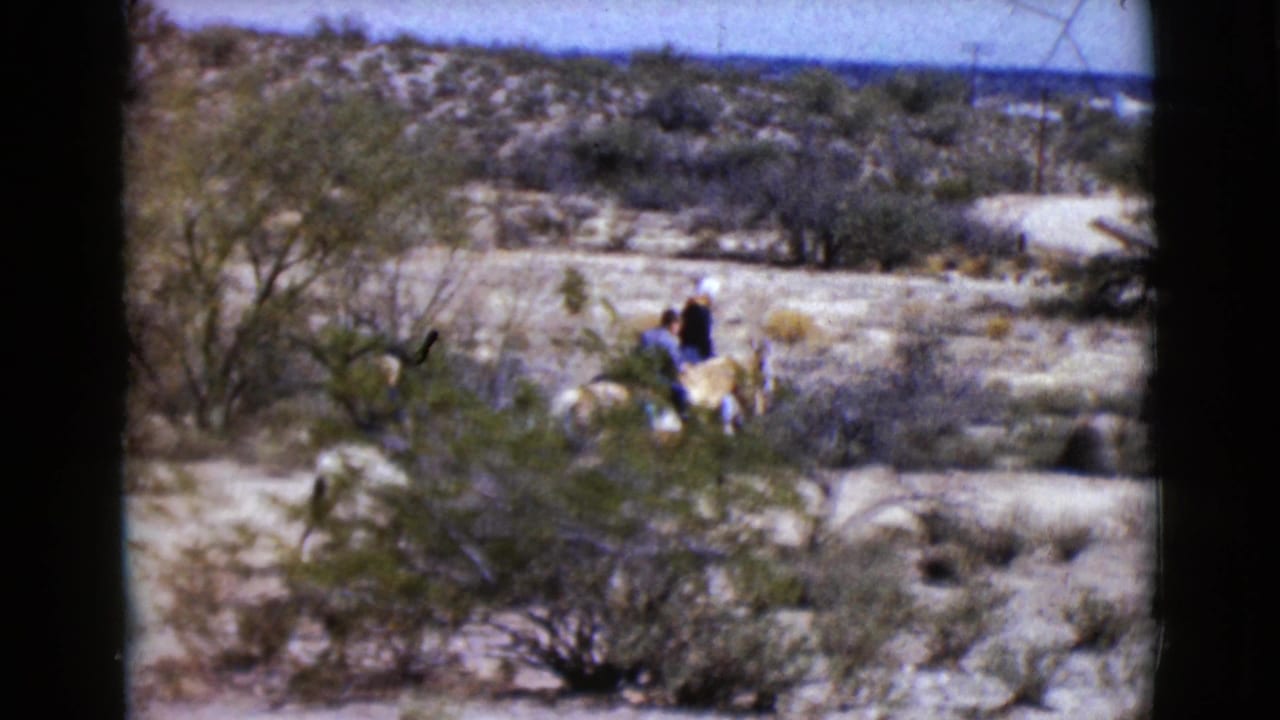 Three riders on horses move through a scrubby desert landscape.
