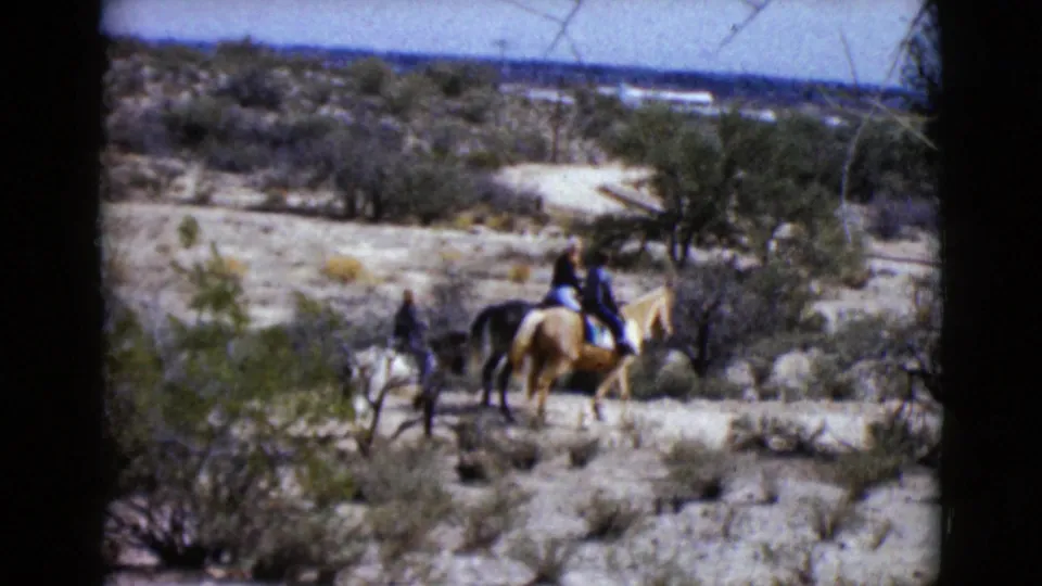 The riders appear closer together on a sandy desert trail, with scrub vegetation and distant open terrain behind them.