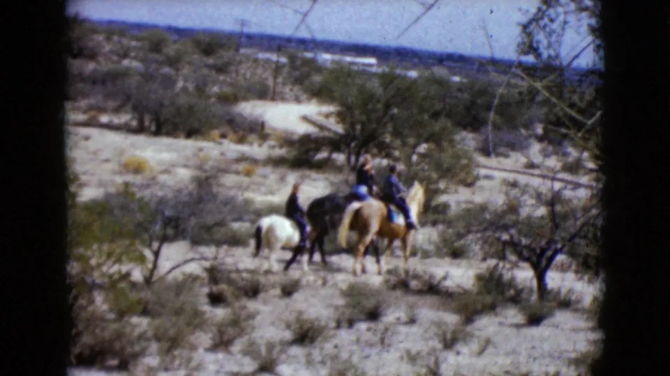 Three riders on light and dark horses pause or move slowly in the Clarksdale, Arizona desert setting from the 1968 8mm footage.