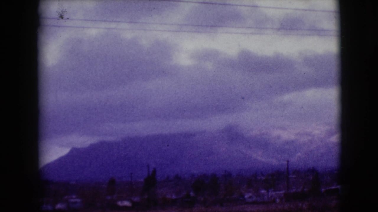 Clouds hang over a distant snow-streaked mountain range beyond a dark roadside foreground.