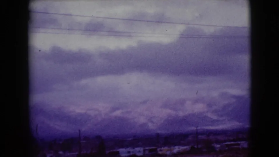 Final 1968 Clarksdale, Arizona frame showing a cloudy winter mountain view with low structures, utility poles, and blue-purple aged film color.
