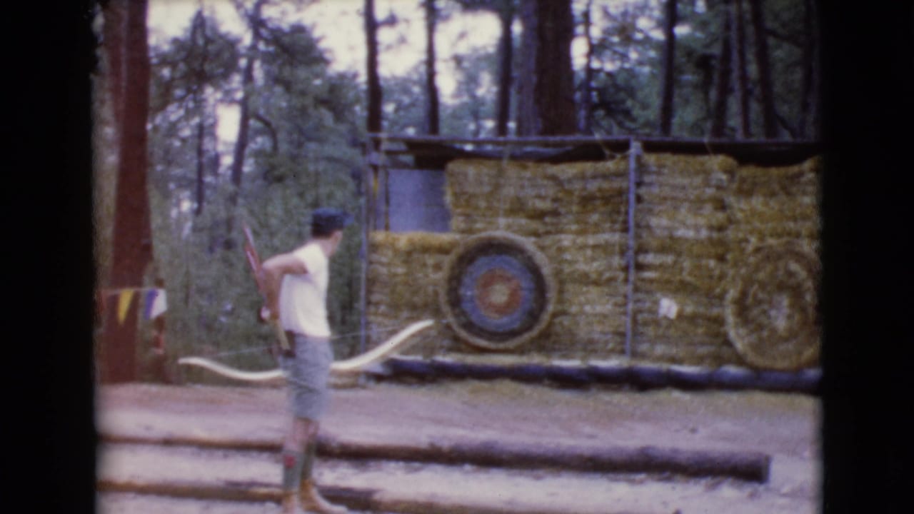 Young man stands with a lowered bow in front of straw archery targets.
