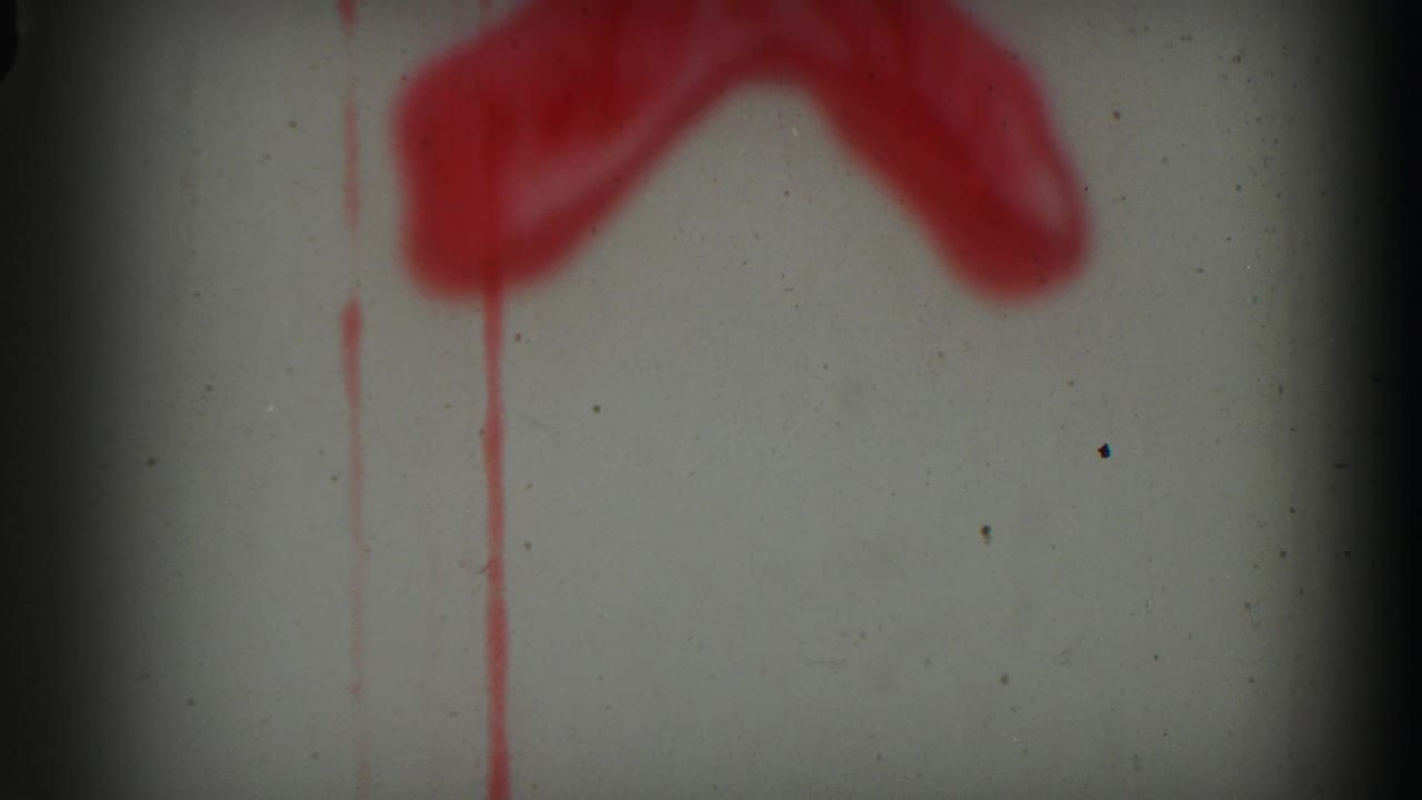 Pale 8mm frame with red painted or leader markings, vertical red drips, dust, and a dark frame boundary.