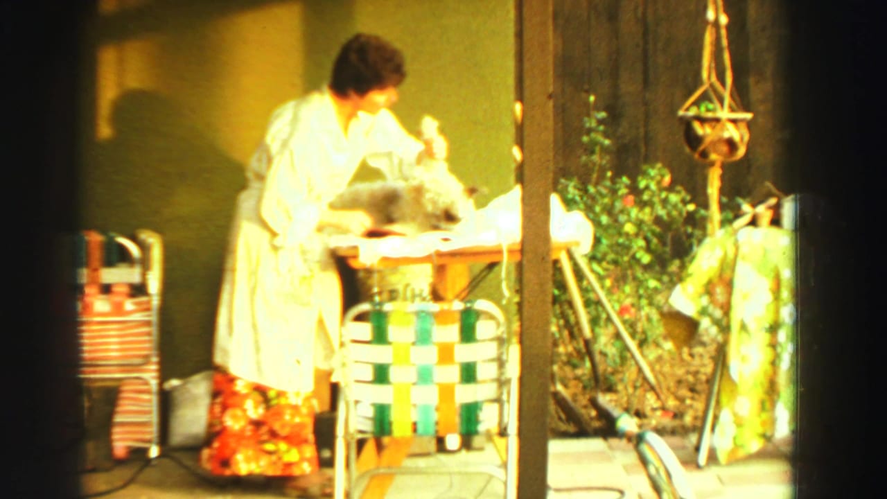 Woman in a white robe trims a fluffy dog on a backyard table.