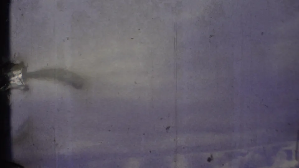 Soft 8mm frame of pale sky and clouds, heavily marked by grain, scratches, and edge shadow.
