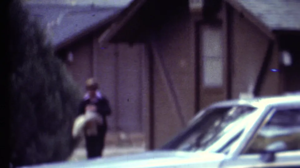 1972 Grand Canyon-area home-movie frame with a woman walking near a rustic building and a parked car in front.