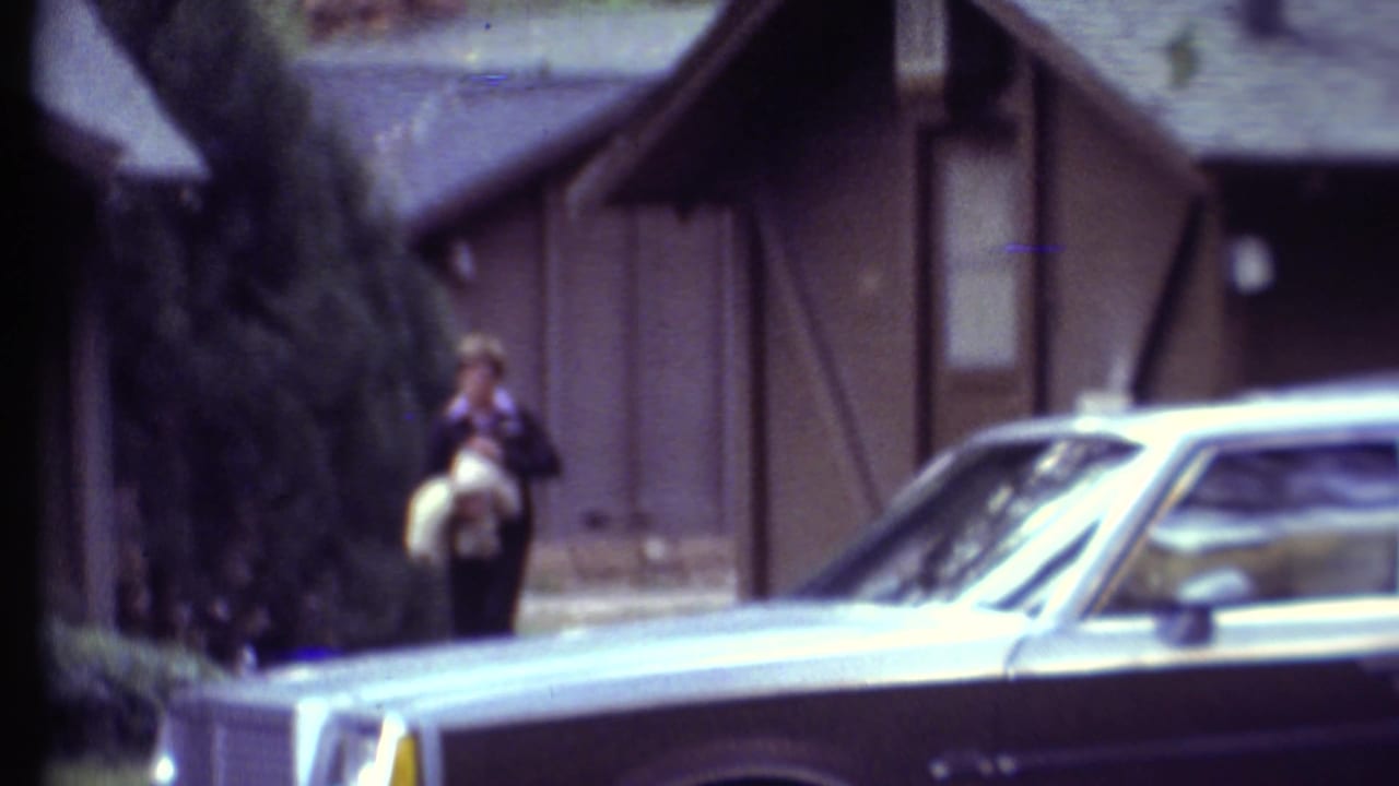 1972 Grand Canyon campground view with a man near wood-sided cabins and a parked station wagon in the foreground.