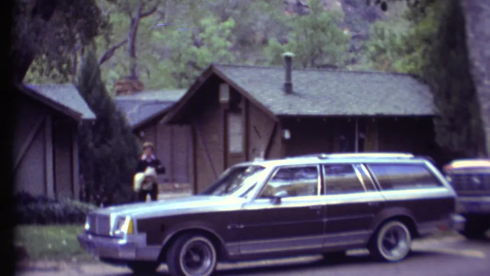 1972 Grand Canyon campground footage showing a man by rustic cabins, trees, grass, and a station wagon parked along the road.