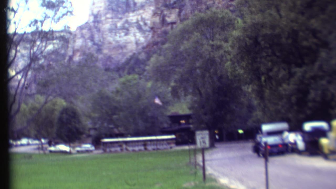 1972 8mm travel frame showing green park grounds, roadside signs, parked cars, trees, and cliffs in the supplied Southwest park location.