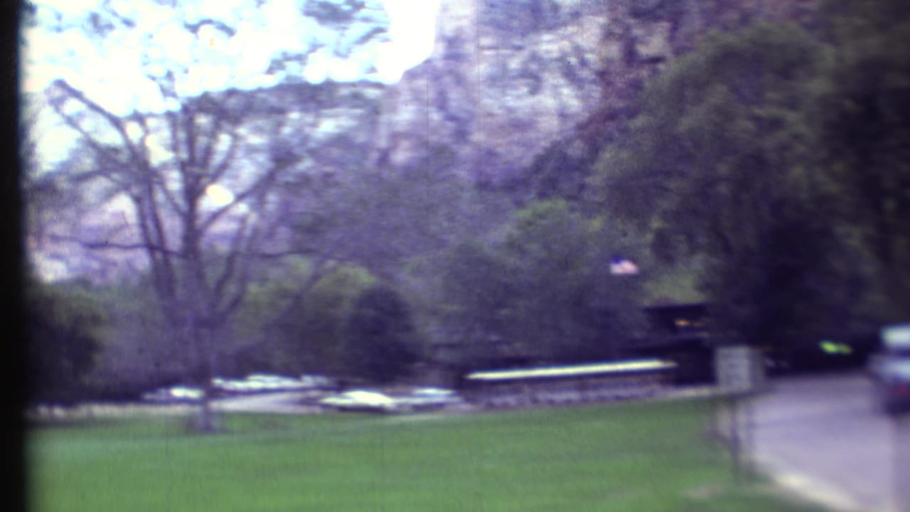 Trees and lawn beside a park road with parked cars and cliffs in the background.