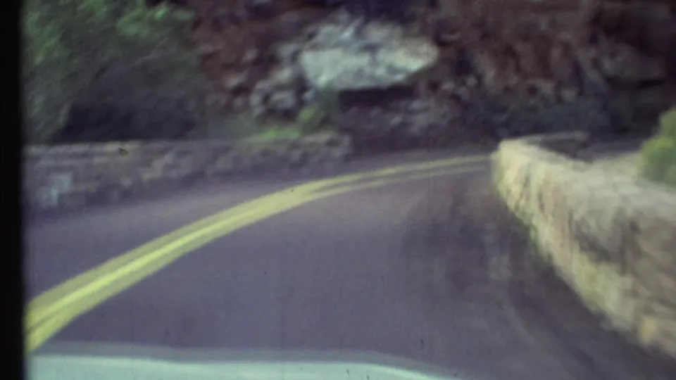 1972 Grand Canyon driving view of a paved road curving between rocky slopes and a low stone roadside wall.