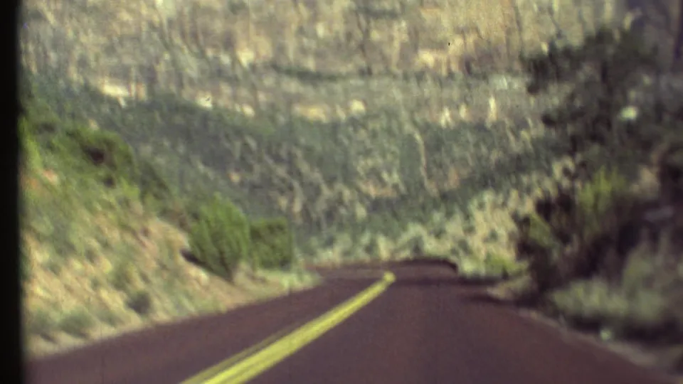 1972 Grand Canyon travel footage looking forward along a paved road through dry vegetation and rocky canyon terrain.