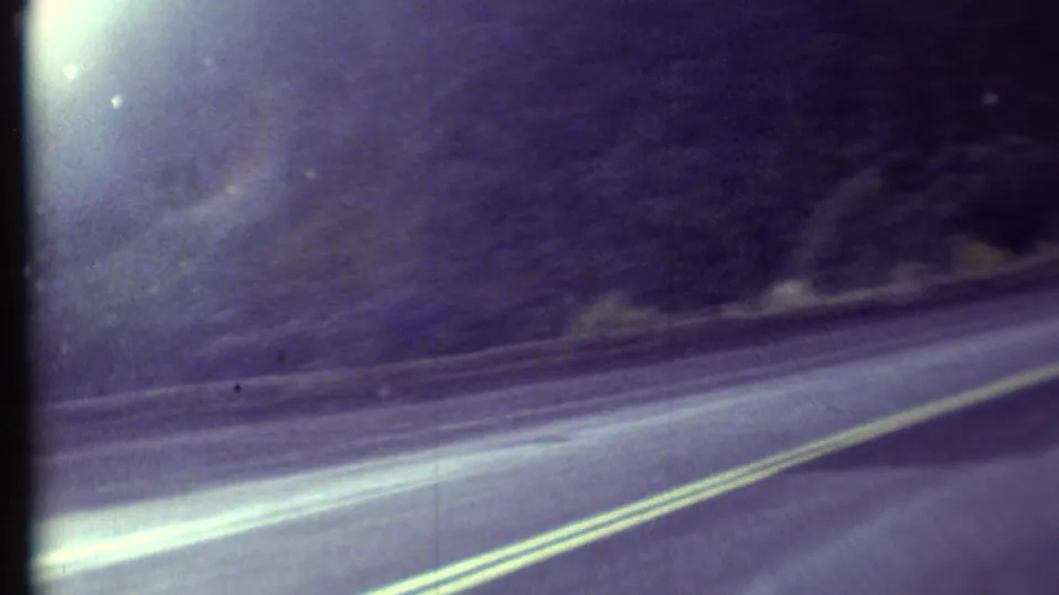 1972 dashboard view shows a winding Arizona road, double yellow lines, roadside slope, and faded 8mm color.