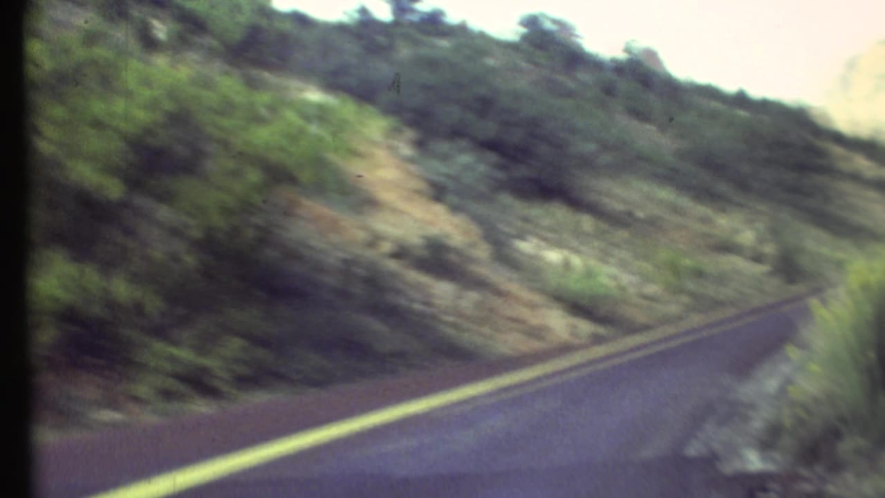 Winding paved road with double yellow lines passing through scrubby canyon slopes.