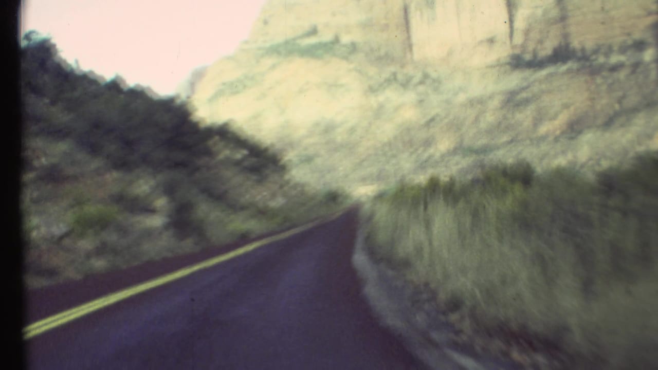 Road bending right beside brush and pale canyon rock in a dry landscape.