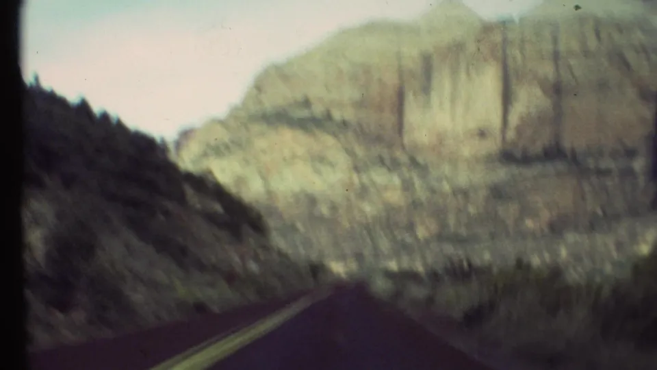 Motion-blurred Grand Canyon driving view with roadway, yellow center line, dark slope, and pale rock wall ahead.