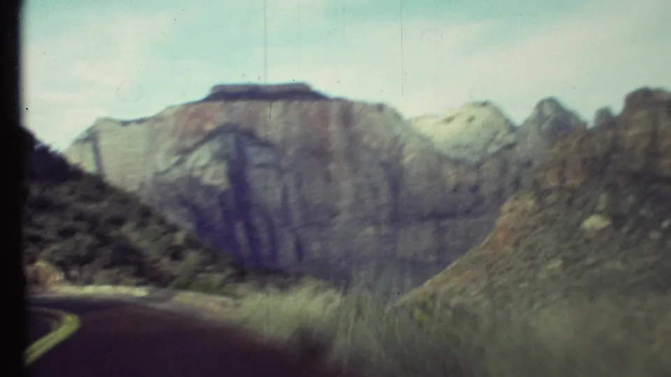 Soft 8mm Grand Canyon road view with the lane disappearing at lower left and layered canyon walls across the horizon.