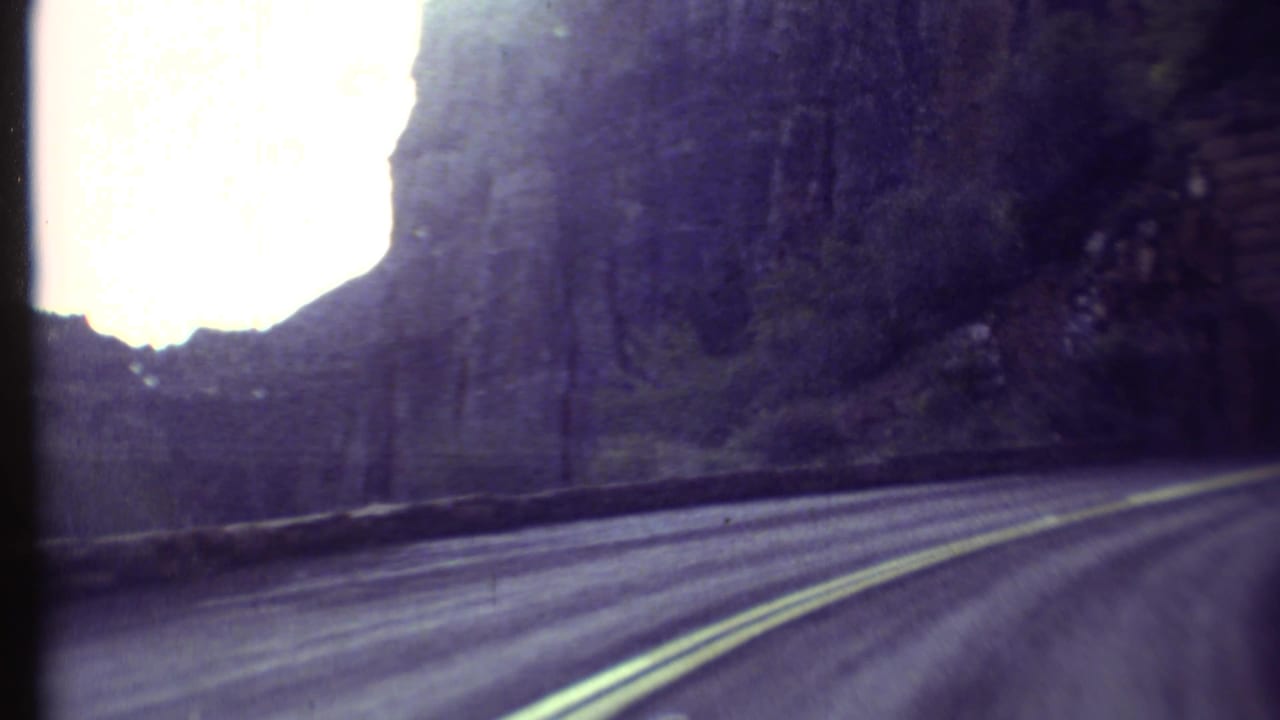 1972 Grand Canyon 8mm frame showing a road curving along rock walls toward a dark tunnel entrance.