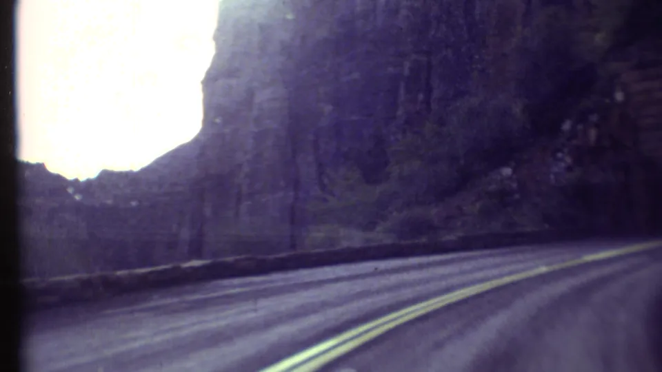 1972 Grand Canyon 8mm frame showing a road curving along rock walls toward a dark tunnel entrance.