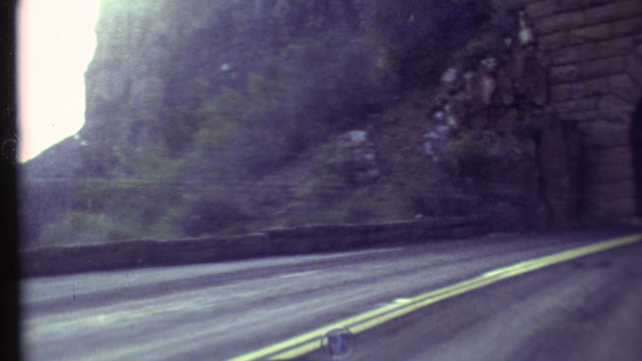 Roadway nears a brick-lined tunnel entrance with rock and greenery beside it.