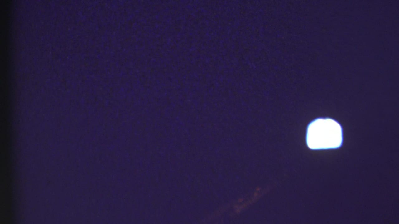 Dark 8mm frame from the 1972 Grand Canyon travel footage, showing a small bright light against a blue-purple exposure.