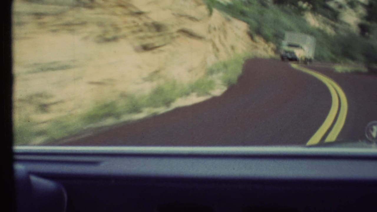 Windshield view of a winding road beside a pale rock wall with a truck farther ahead.