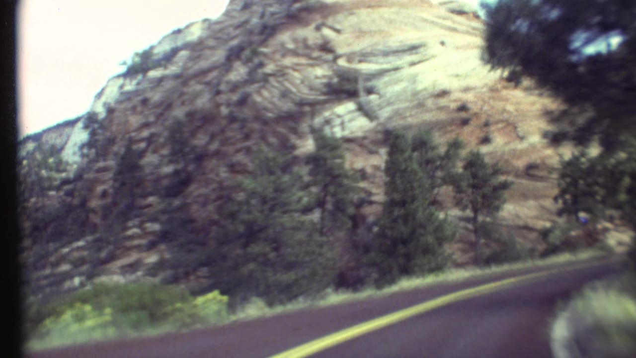Rocky canyon wall beside a curving road, filmed from a moving car.