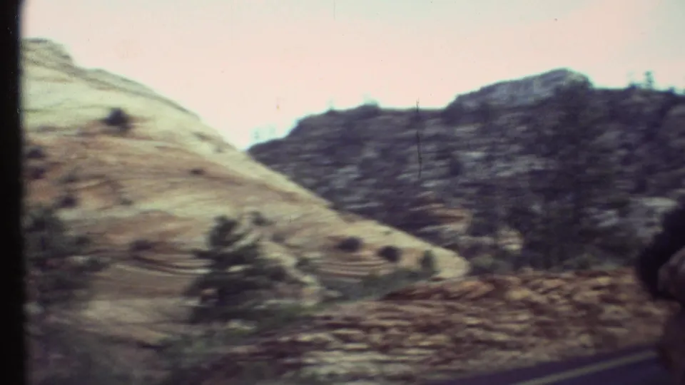 Grand Canyon, Arizona 8mm frame with layered hills, roadside trees, a narrow road edge, and soft exposure typical of home-movie travel footage.