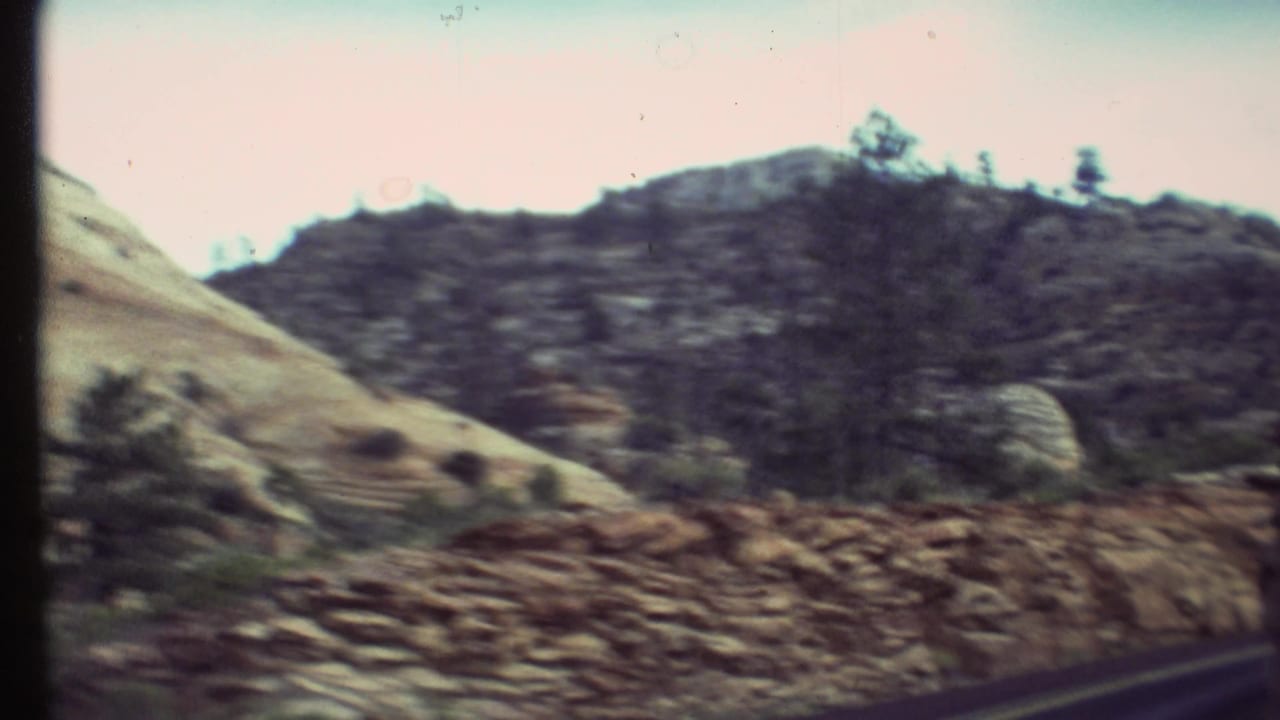1972 Grand Canyon-area home-movie view of rocky roadside slopes and sparse trees from a moving car.