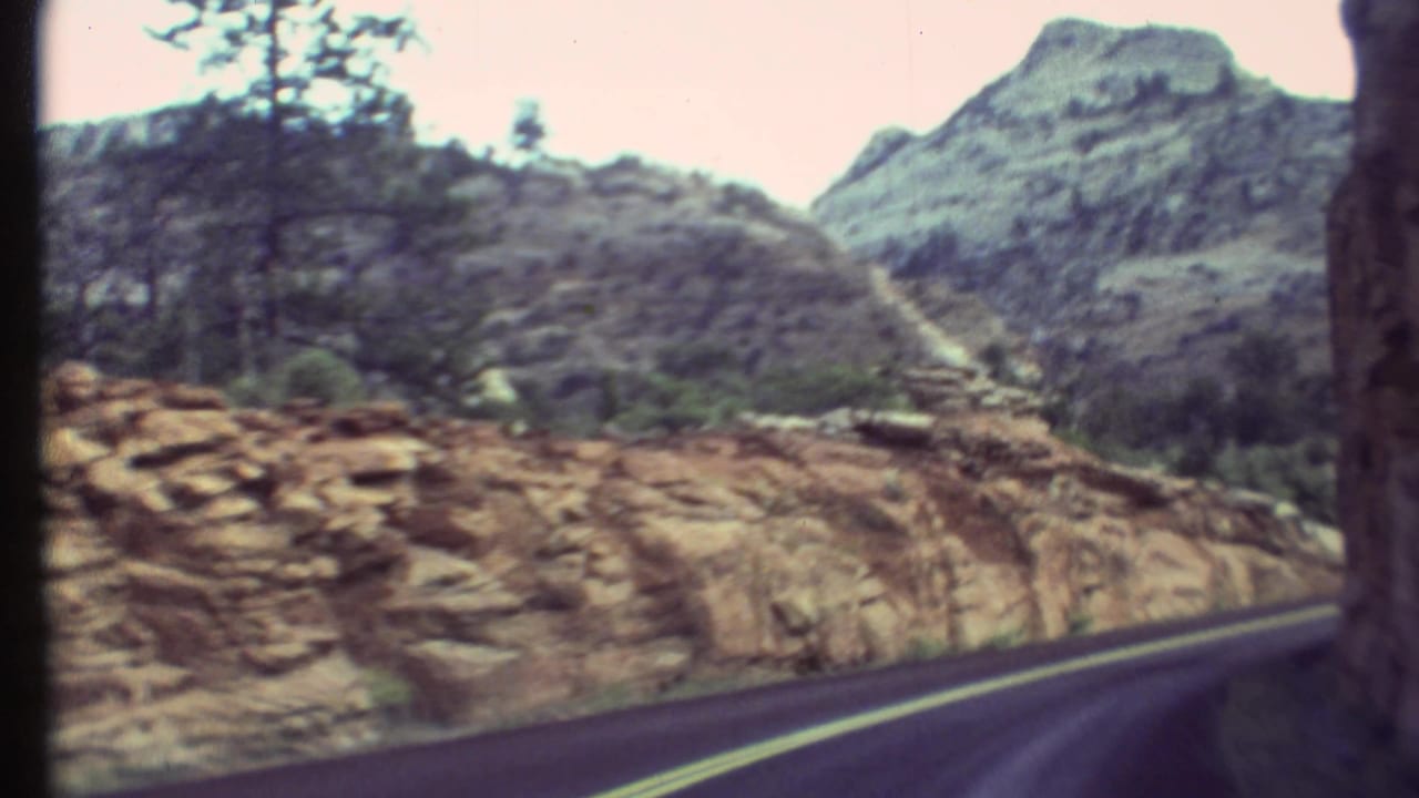 A Grand Canyon, Arizona road curves past layered rock and scrub in this 1972 8mm travel view.