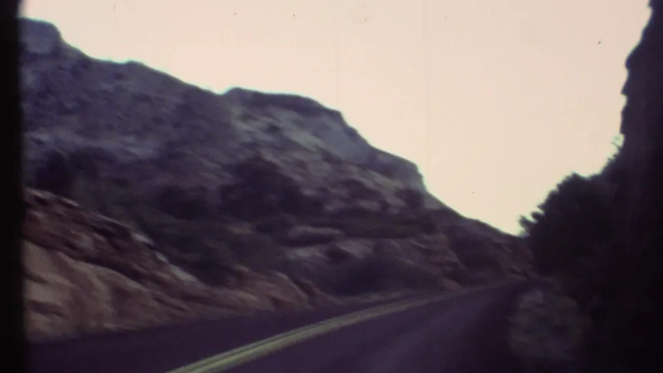 1972 Grand Canyon driving shot showing a narrow road between steep rock faces and shadowed canyon slopes.