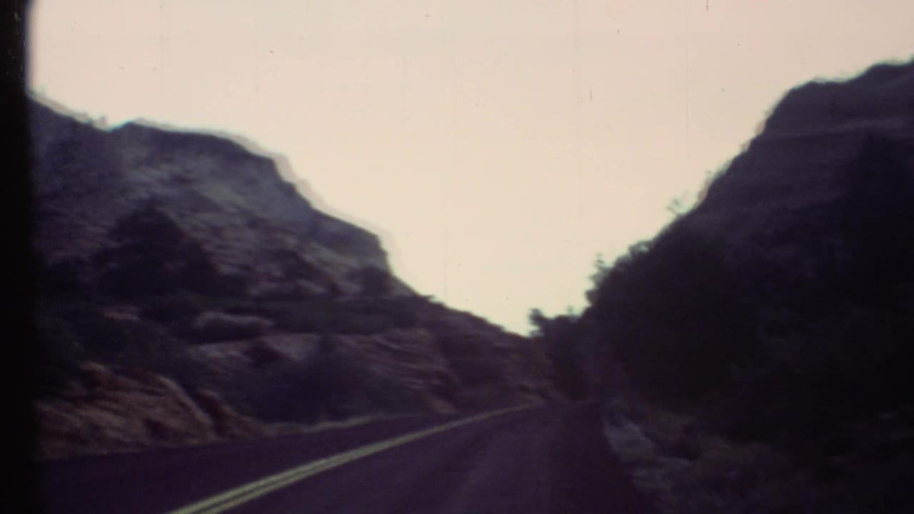 1972 8mm road view in the Grand Canyon area, with a blacktop road passing between rugged rock formations.
