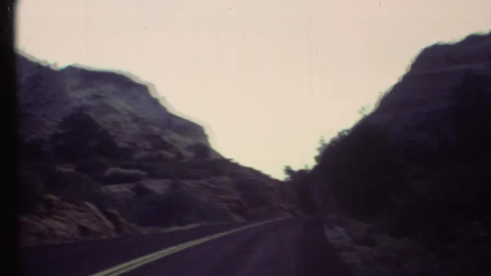 1972 8mm road view in the Grand Canyon area, with a blacktop road passing between rugged rock formations.