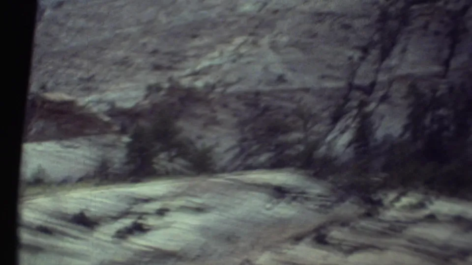 1972 Grand Canyon travel footage showing a blurred rocky wall, sparse trees, and pale roadside ground from inside a moving vehicle.