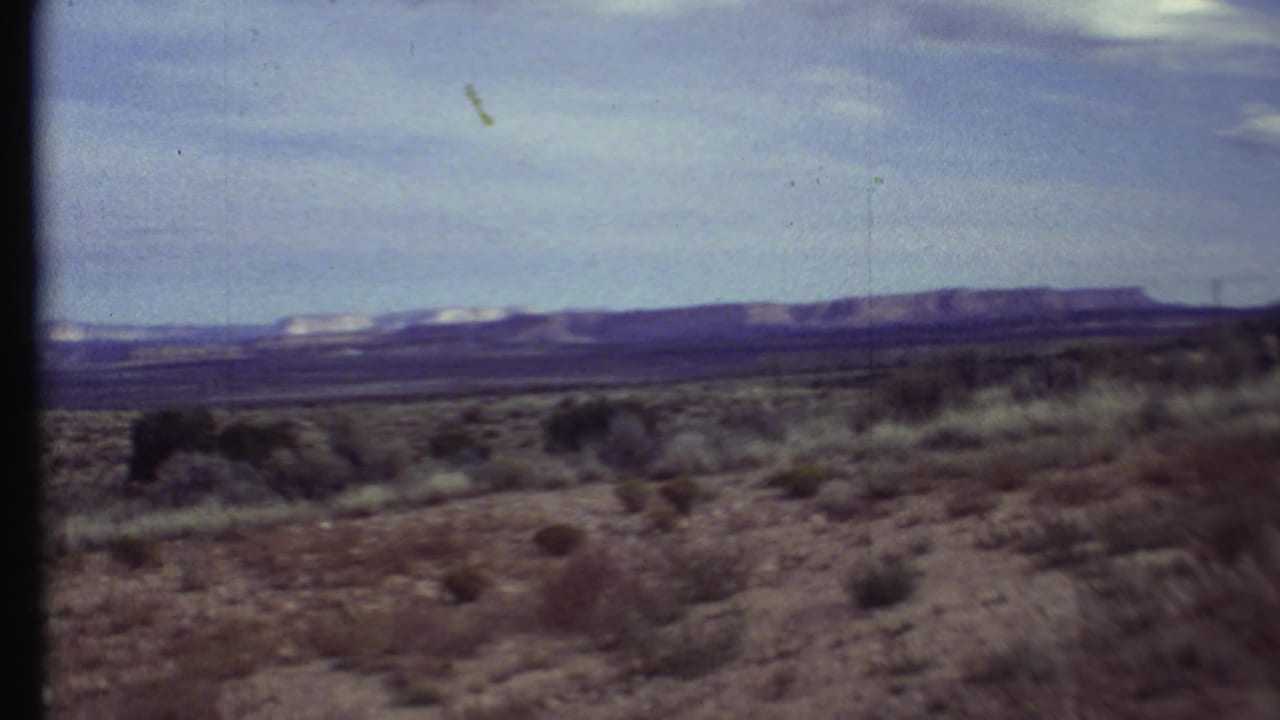1972 8mm Grand Canyon-region view of dry bushes and open desert plain leading to distant mesa-like ridges.