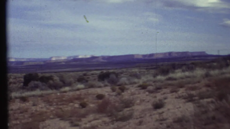 1972 8mm Grand Canyon-region view of dry bushes and open desert plain leading to distant mesa-like ridges.