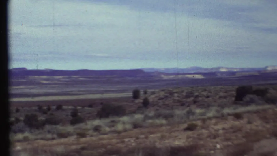 Soft 8mm frame of the Arizona desert basin, with foreground brush and layered distant hills across the horizon.