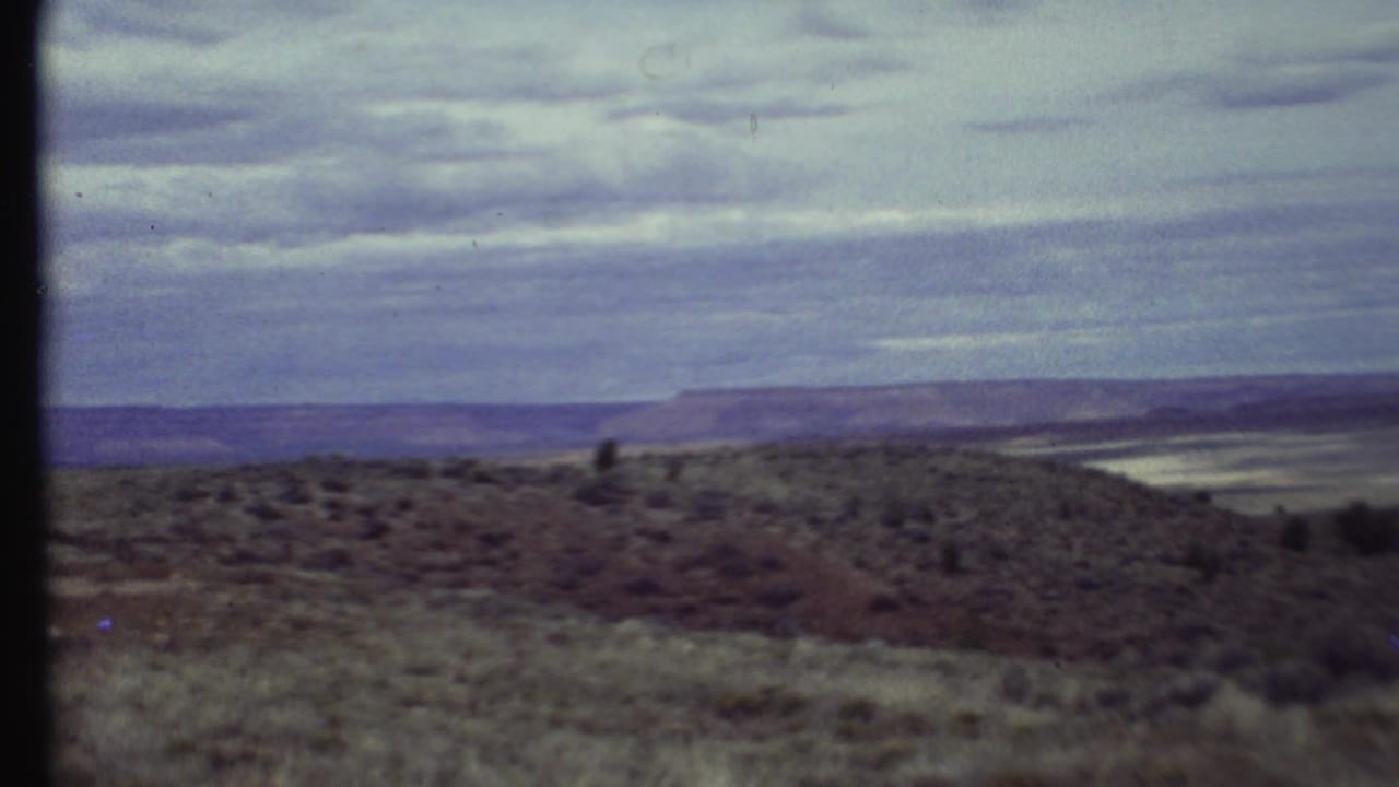 Distant mesas and scrubland beneath a cloudy sky, bordered by dark film edges.