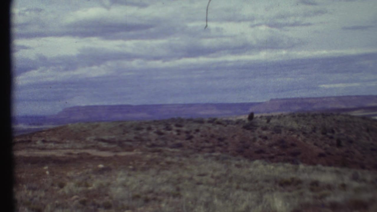 Scrubby hillside and distant plateau under a cloudy sky, framed by film borders.