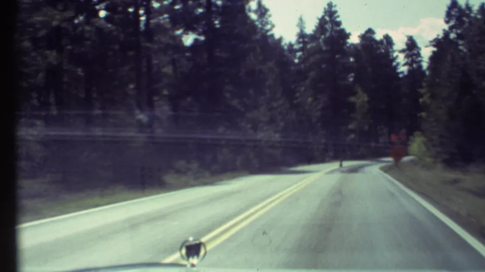 Windshield view of a paved forest road in the Grand Canyon area, captured on faded 1972 8mm home-movie film.